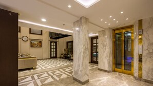 Um saguão de hotel com piso de mármore, um sofá, um relógio e um elevador.