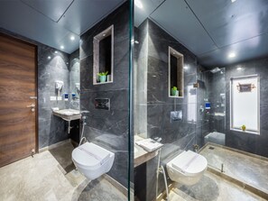 A modern bathroom with a marble floor, a wooden door, a glass shower enclosure, and a white toilet. - Hotel Sapphire House Paharganj (New Delhi)