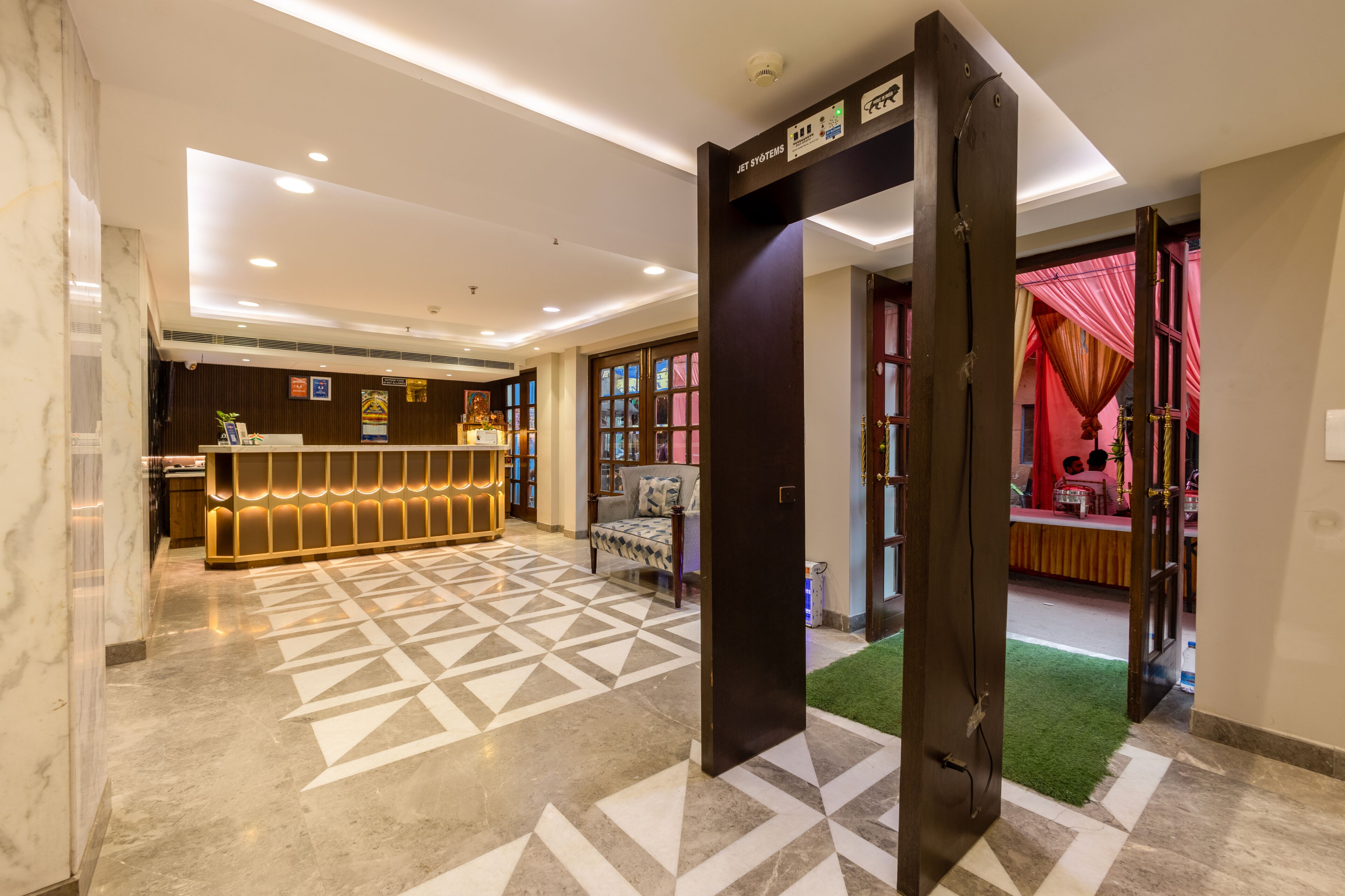 A hotel lobby with a reception desk, patterned floor, and a door leading to a room with a red curtain.