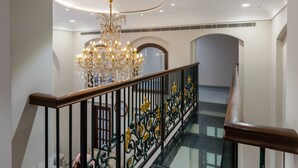 Uma escadaria imponente com corrimão de vidro, um candelabro e piso estampado.