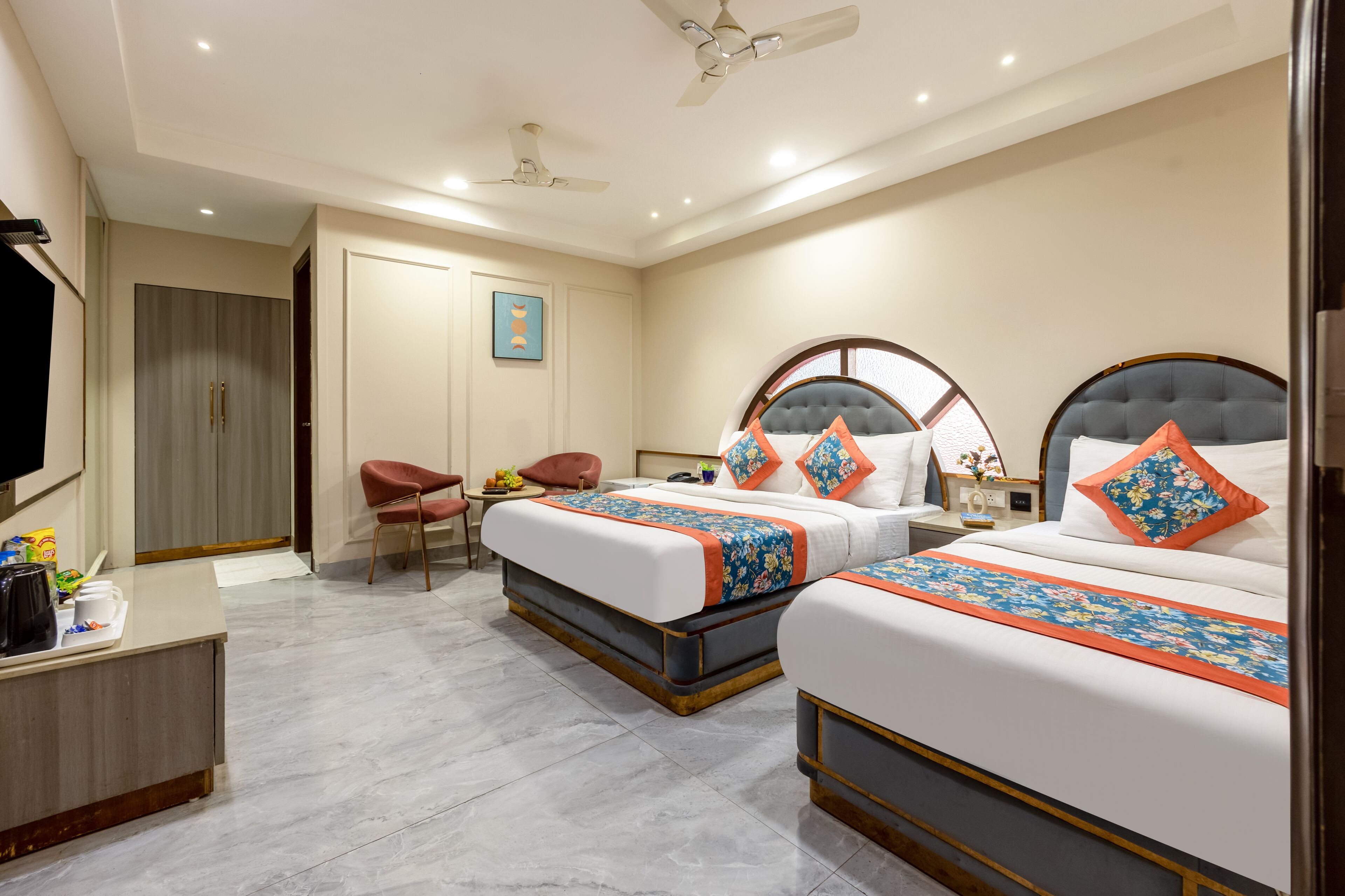 Une chambre d’hôtel avec deux lits, un bureau, une chaise, une armoire et un ventilateur de plafond.