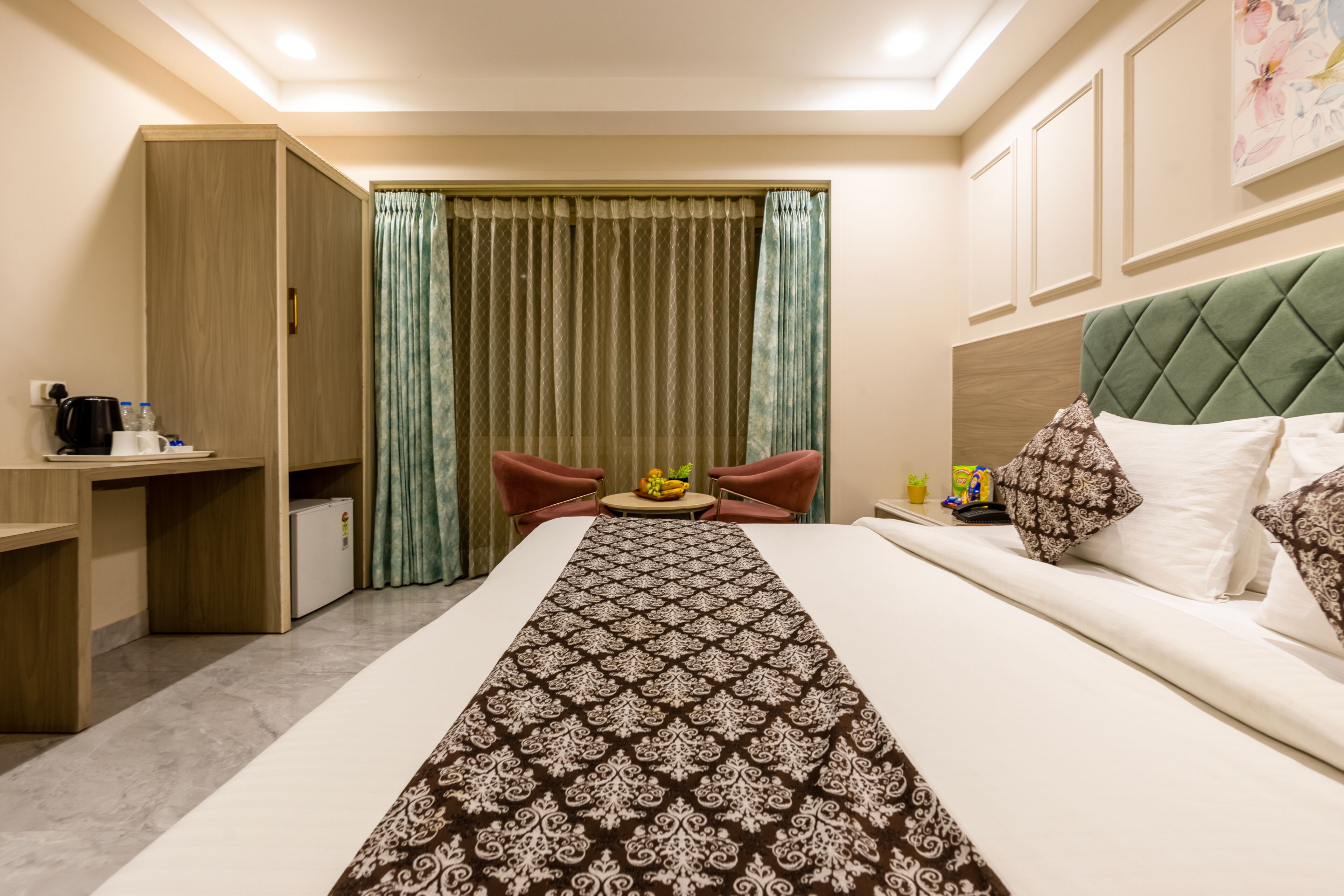 A hotel room with a bed, a desk, a chair, a small table with fruit, and a wardrobe.