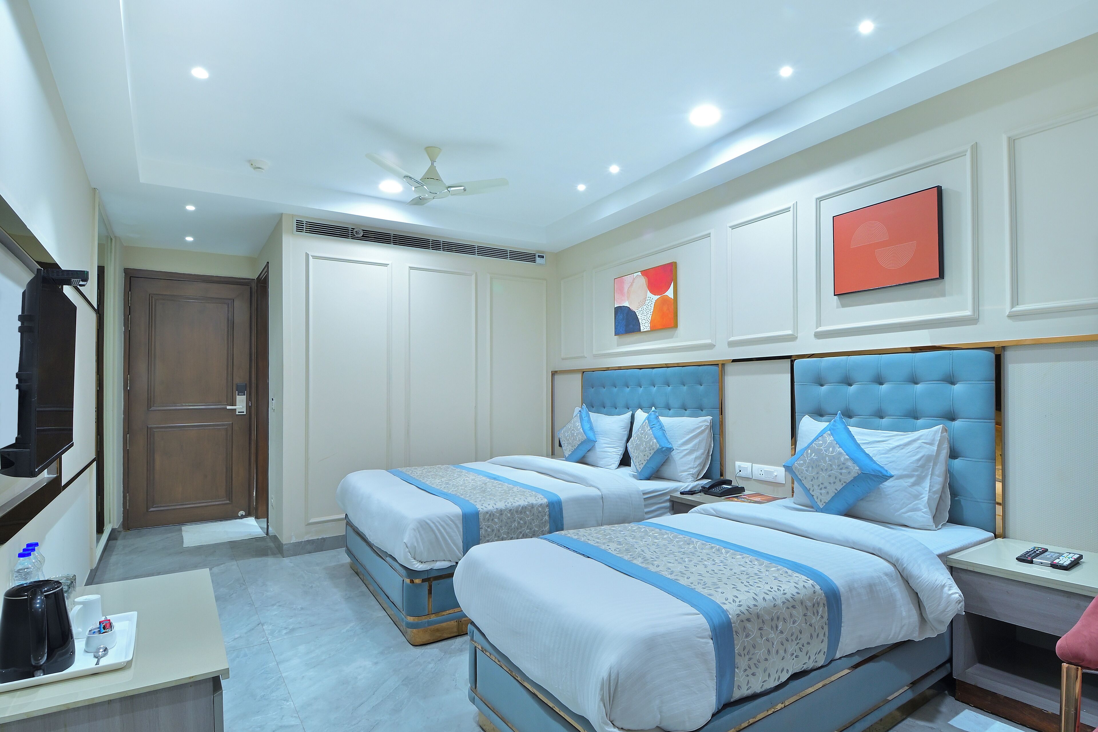 A hotel room with two beds, a desk, a chair, a TV, and artwork on the walls.