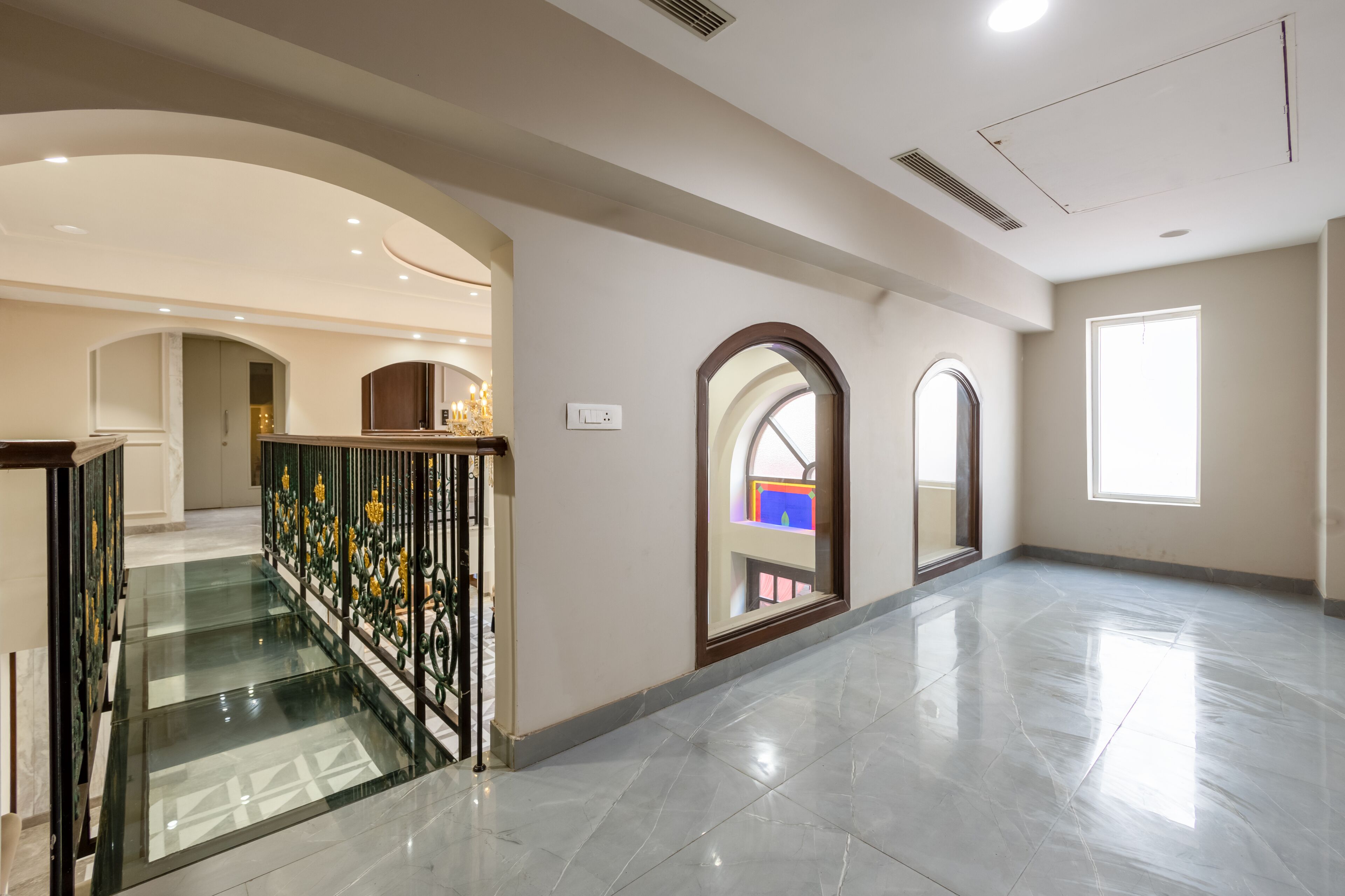 A spacious interior with a glass staircase, arched doorways, and a large window.