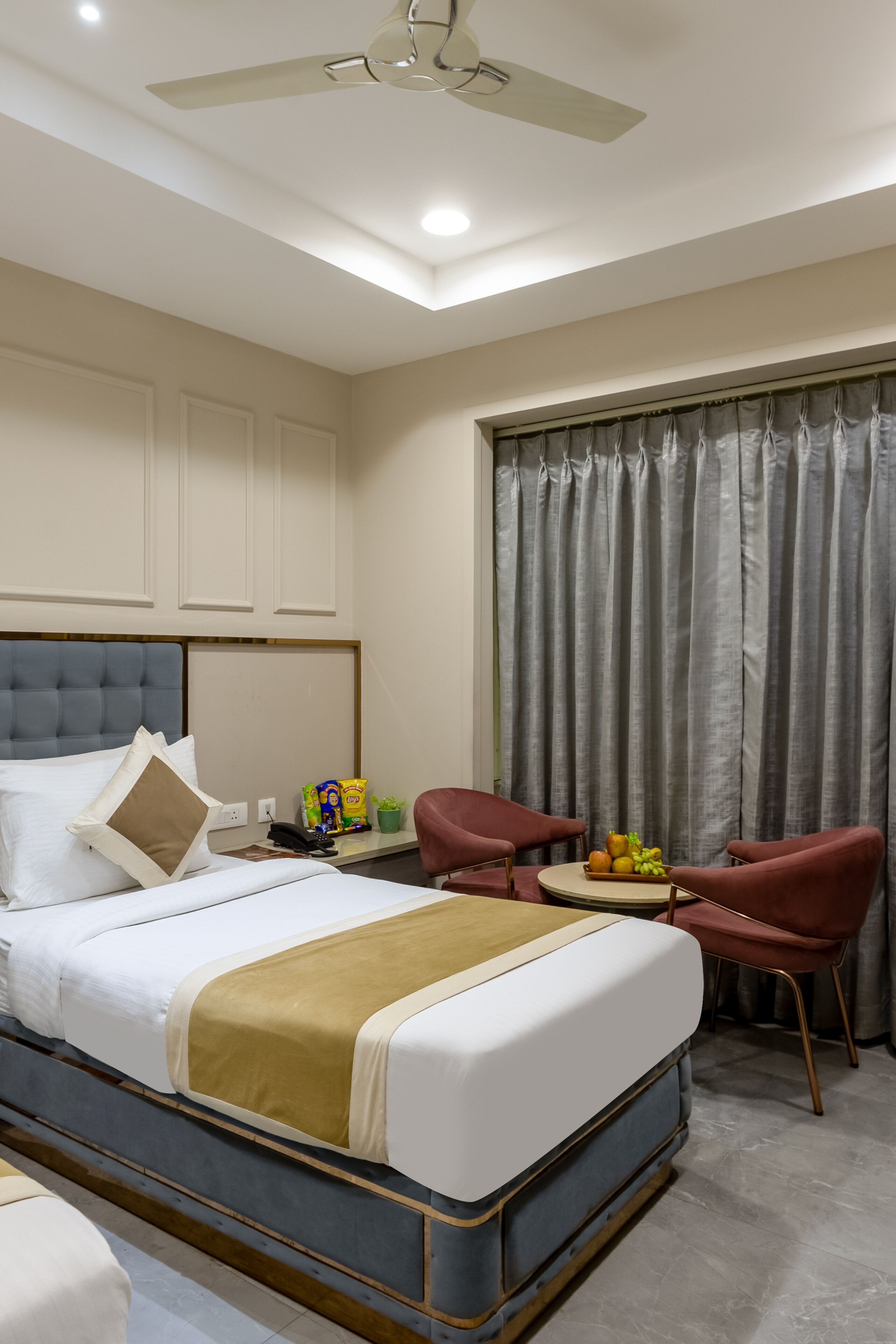 A hotel room with a bed, a desk with a chair, a ceiling fan, and a window with curtains.