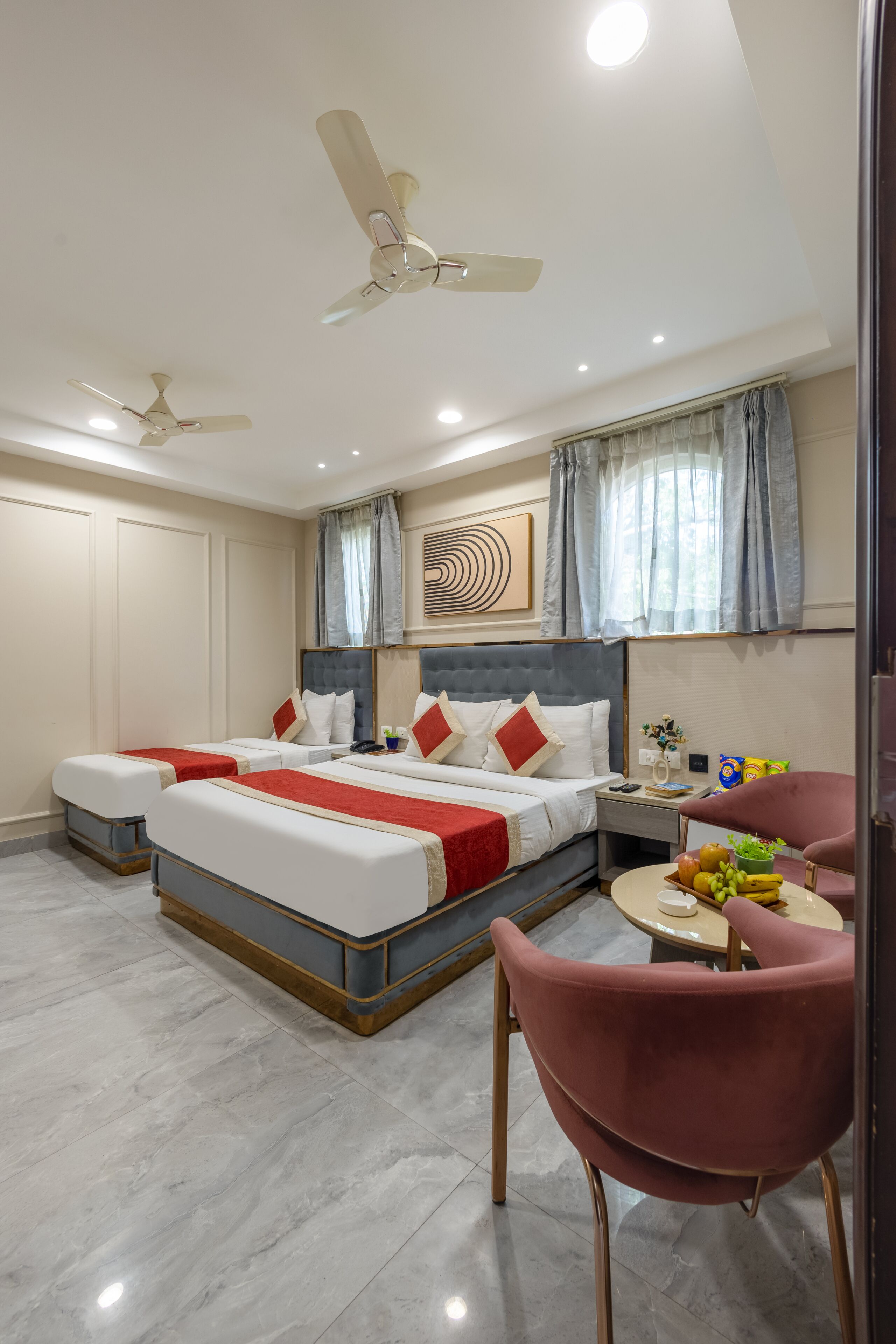 A hotel room with a bed, two ceiling fans, a dining table with chairs, and a fruit bowl.