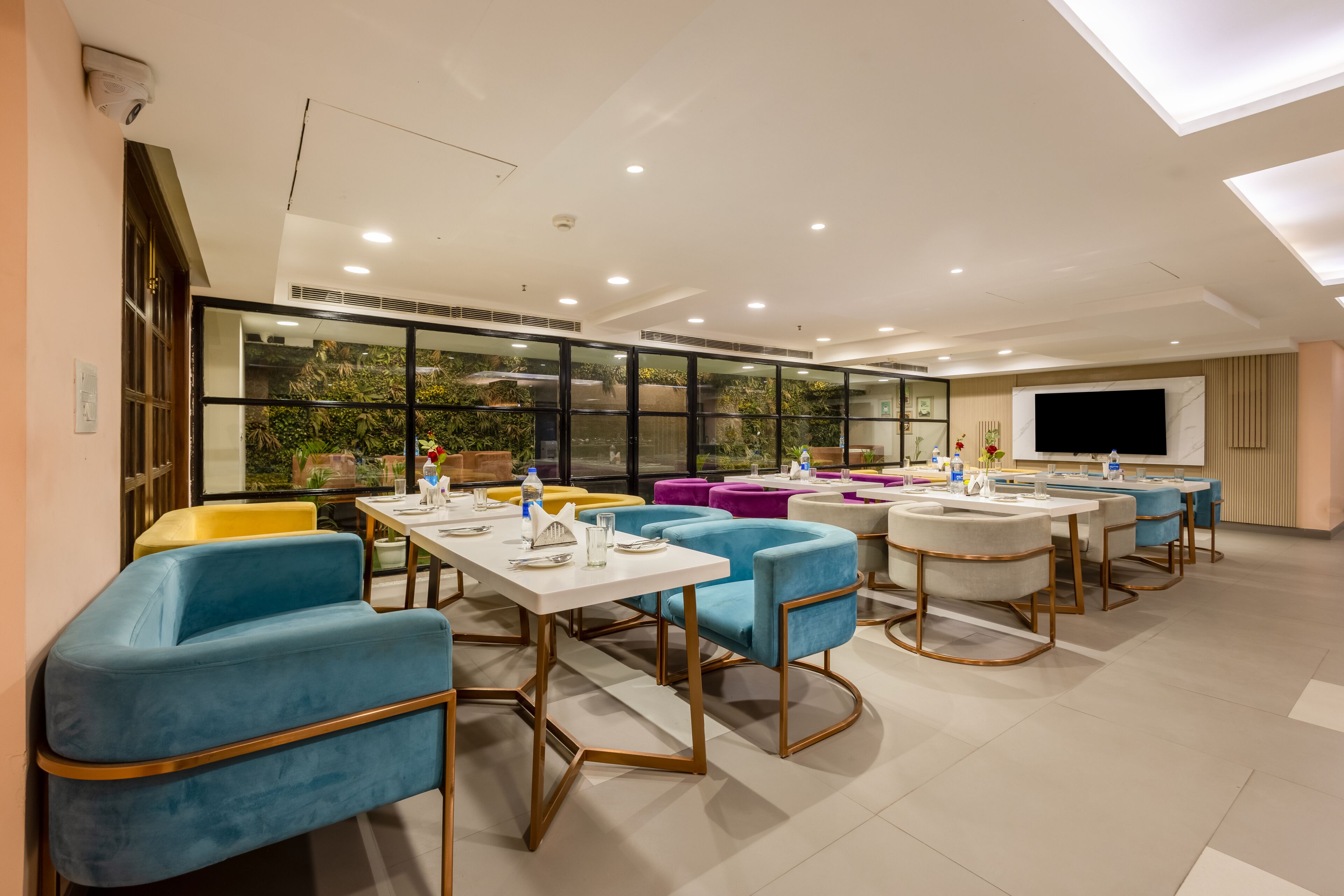A modern dining area with tables and chairs, large windows, and a flat-screen TV.