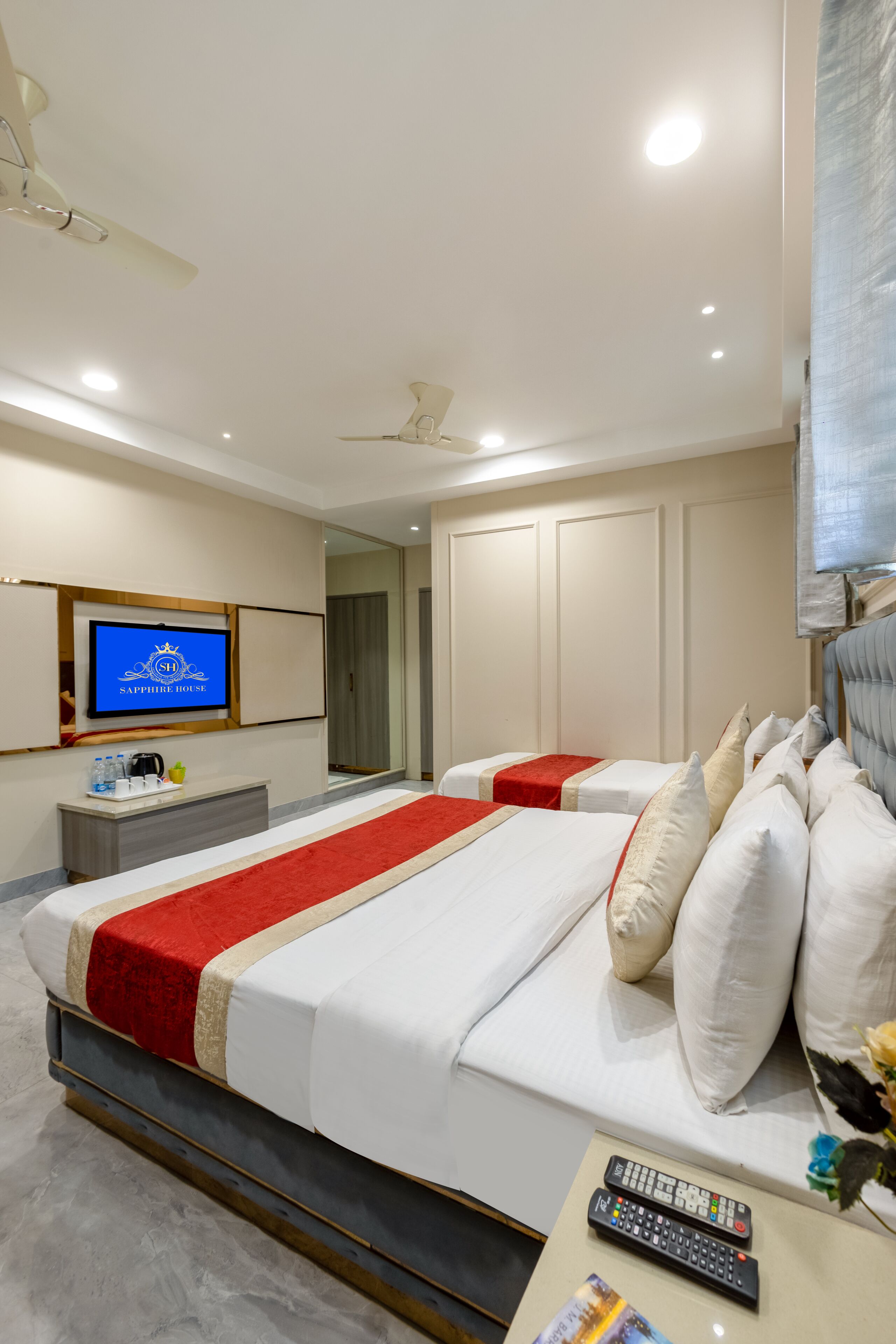 A hotel room with two beds, a TV, a desk with a remote, and a mirror.
