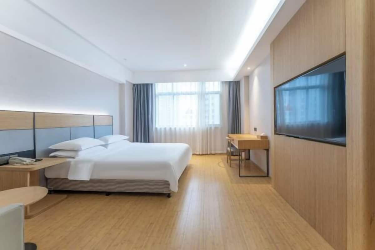 A hotel room with a bed, bedside table, TV, and a desk with a chair.