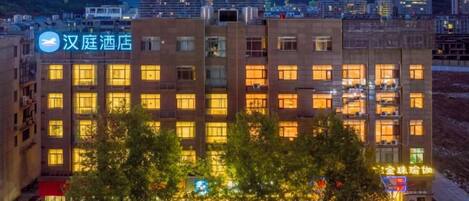 A multi-story hotel building with illuminated windows, a visible sign for the hotel, and a view of the surrounding cityscape.