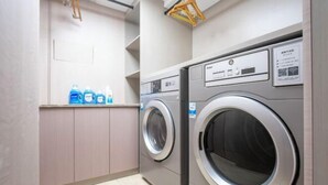 A laundry room with two front-loading washing machines, a shelf with detergent bottles, and a wooden drying rack. - HanTing Hotel (Taizhou Sanmen) (Sanmen)