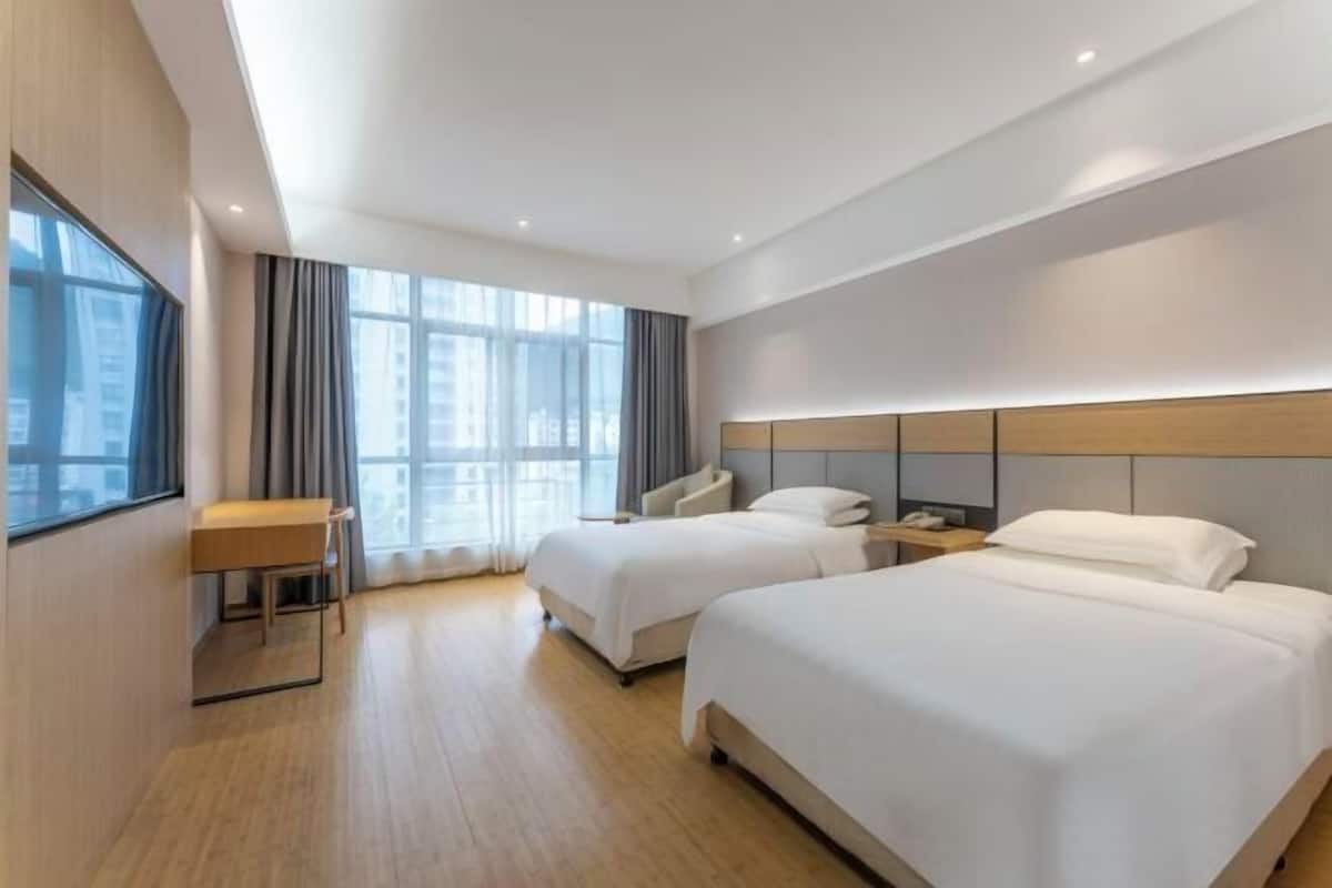 A hotel room with two beds, a desk, and a large window.