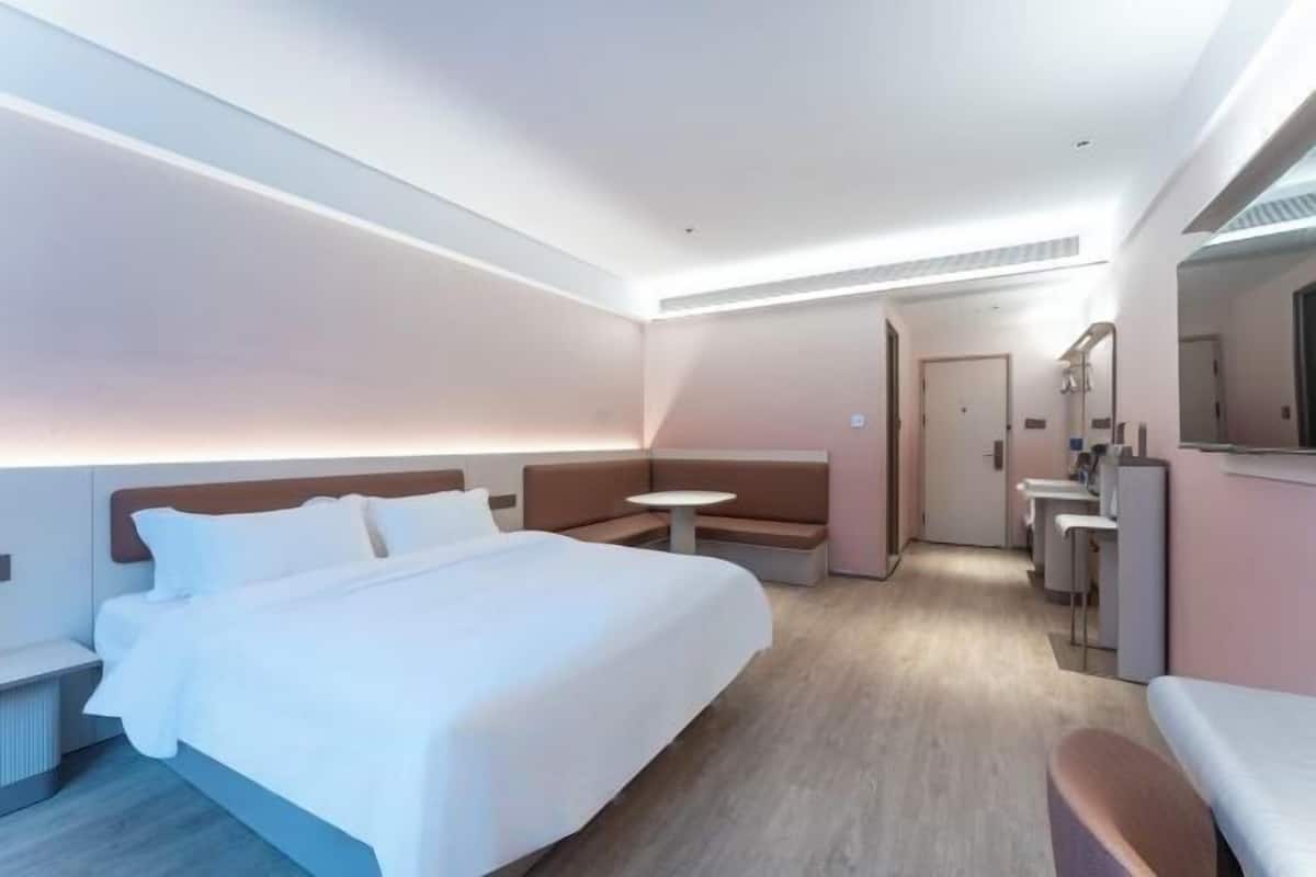 A modern hotel room with a large bed, a small round table, a sofa, and a desk with a chair.
