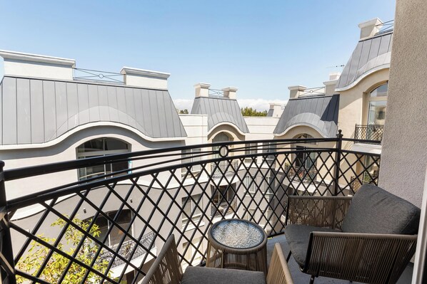 A balcony with wicker furniture and a glass table, overlooking a building with unique architecture and a clear sky.