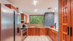 Een keuken met houten kastjes, roestvrijstalen apparatuur, een raam met uitzicht op groen en een granieten aanrecht.