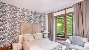 Een slaapkamer met een bed, nachtkastje, lamp en uitzicht op groen via een schuifdeur.