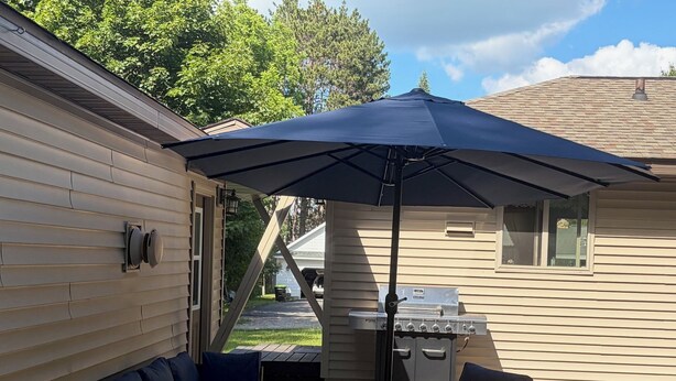 En overdækket terrasse med grill, udendørs møbler og et mønstret gulv.