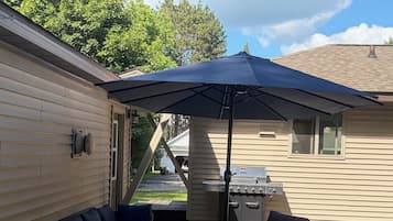 A covered patio area with a grill, outdoor furniture, and a patterned floor.