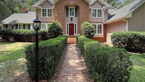 Une maison à deux étages avec une façade en briques, une porte d’entrée rouge et un chemin pavé menant à l’entrée.