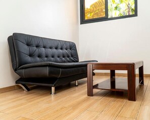Relax in this stylish living room with a leather sofa, coffee table, and floor-to-ceiling window overlooking lush greenery.