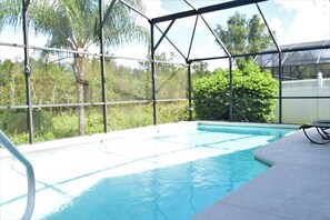 Una piscina con cerramiento de vidrio, rodeada de follaje y árboles.