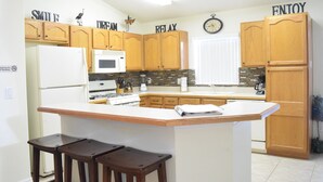 A kitchen with wooden cabinets, a white refrigerator, a microwave, and a clock on the wall. - 2551 Oneida Grantham (Kissimmee)