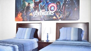 A hotel room with two beds, each with a blue-striped bedspread and matching pillows. A large poster of the Avengers movie is displayed on the wall above the beds. - 2551 Oneida Grantham (Kissimmee)