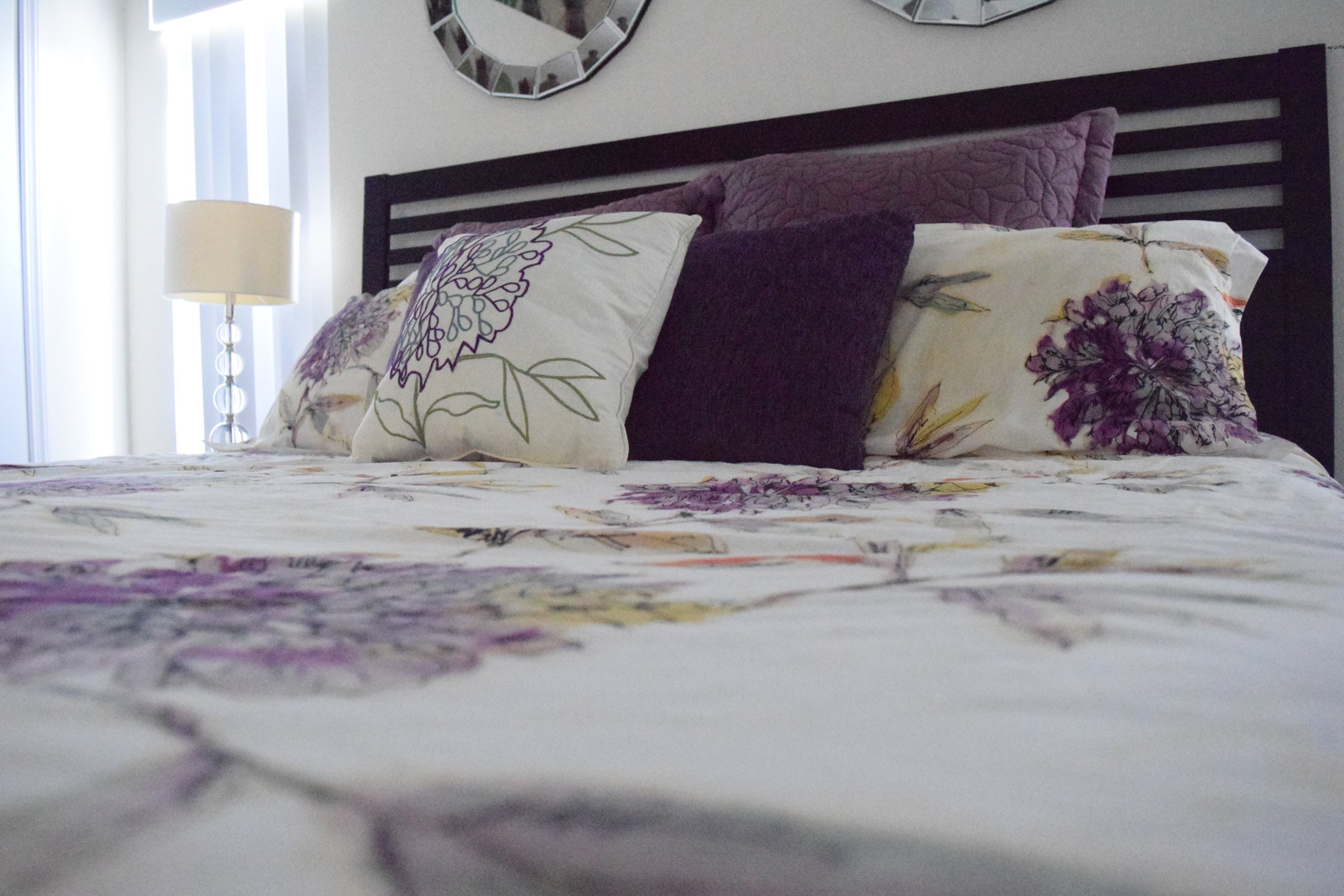 A bed with floral bedding, a dark headboard, and a bedside lamp.