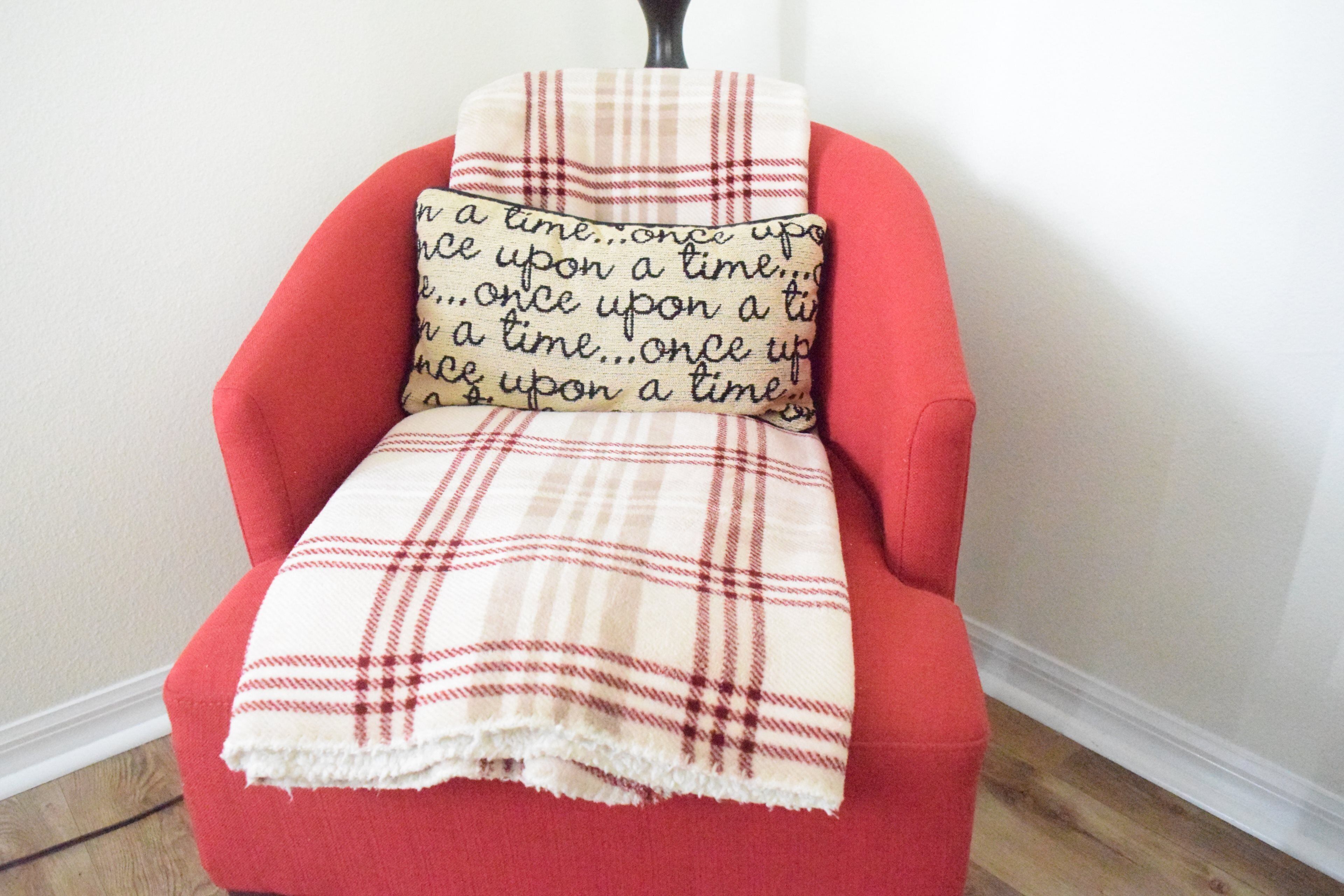A red armchair with a plaid blanket and a pillow with a quote.