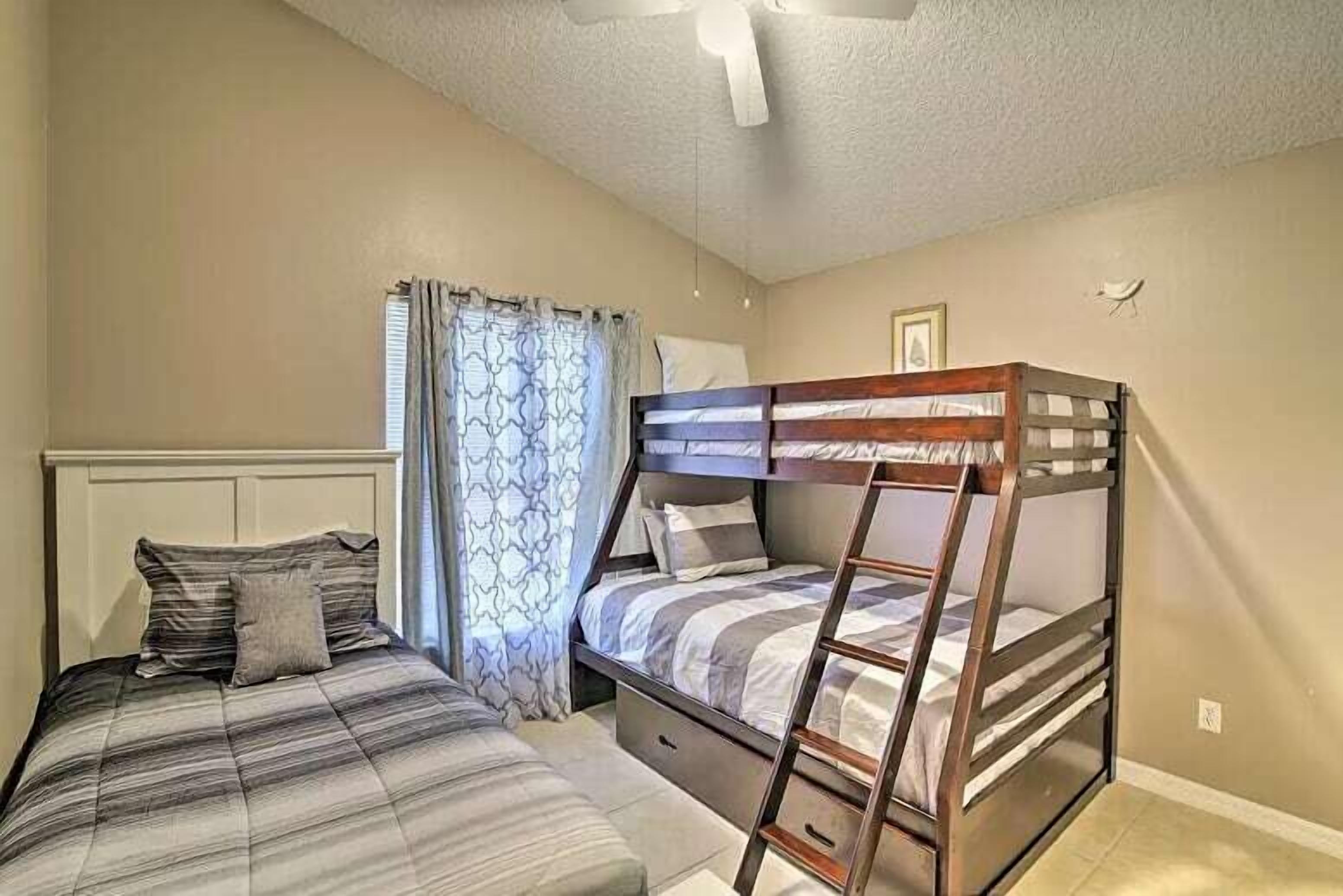 Un dormitorio con una cama litera, una cama individual, un ventilador de techo y una ventana con cortinas.
