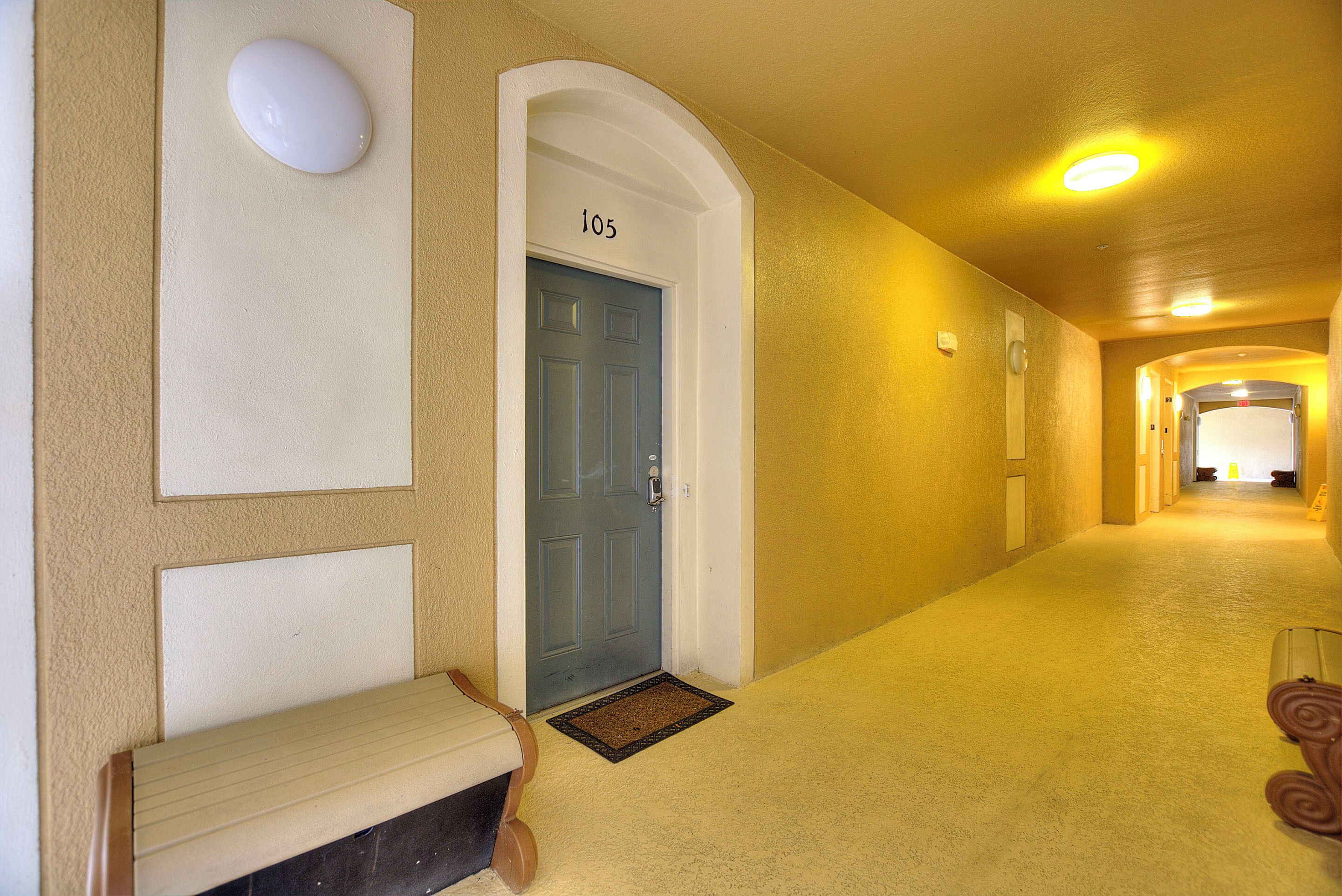 A hallway with a blue door marked "105", a bench, and a doormat.