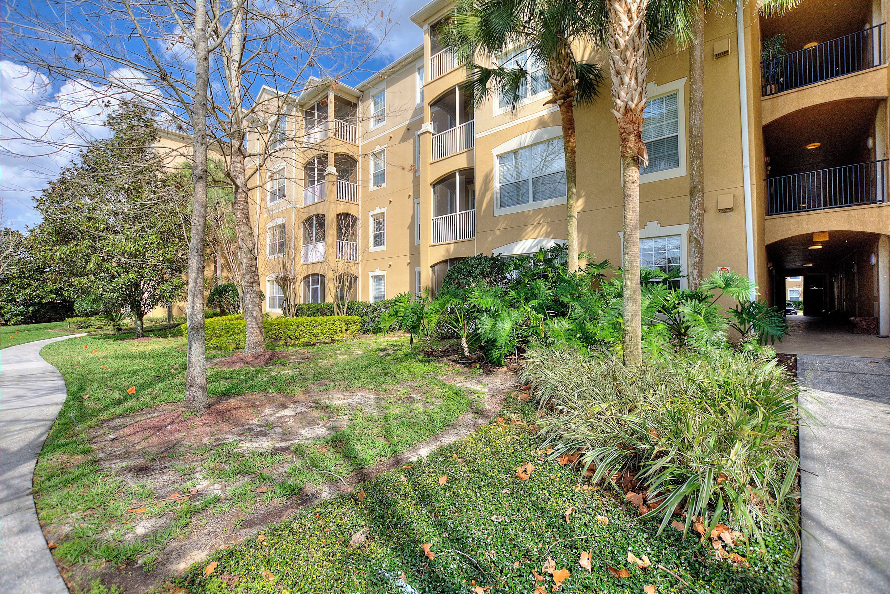 A multi-story building with balconies, a landscaped garden with trees and shrubs, and a paved walkway.