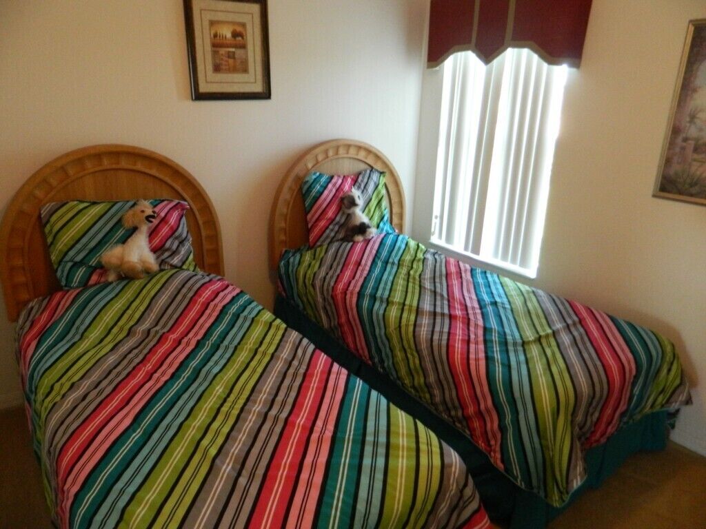 A room with two beds, each with striped bedding. There is a window with vertical blinds, and a framed picture on the wall.