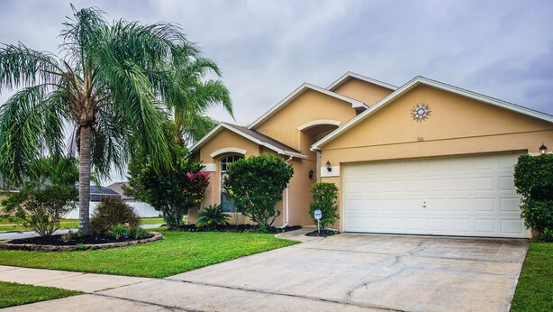 A residential house with a garage, a well-maintained lawn, and a palm tree. - 4 Bed Villa - Eagle Pointe - Kissimmee (Kissimmee)