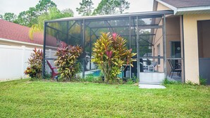 A modern house with a glass-enclosed patio, a well-maintained lawn, and various potted plants. - 4 Bed Villa - Eagle Pointe - Kissimmee (Kissimmee)