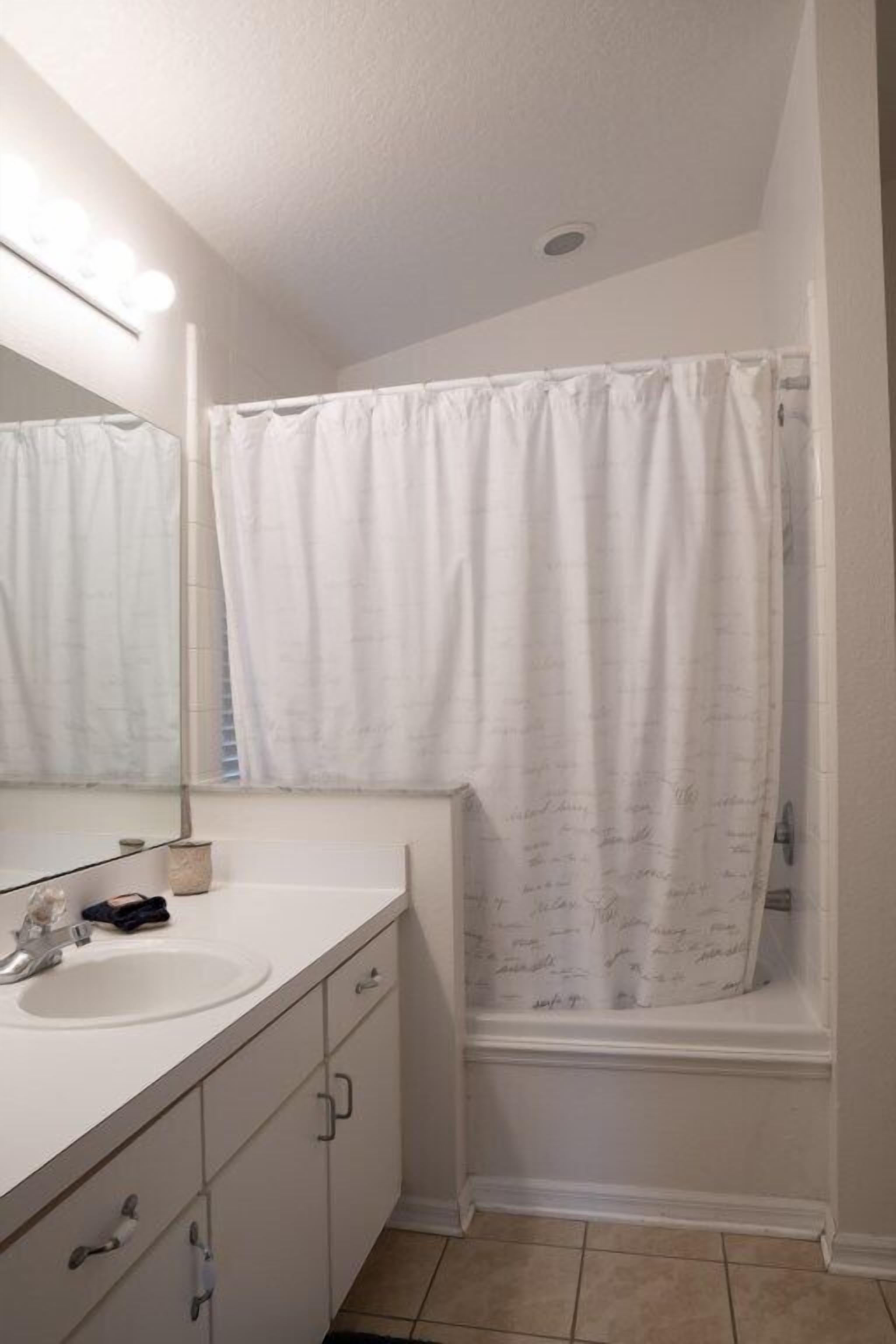 A bathroom with a white sink, mirror, and shower curtain.