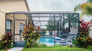 A glass-enclosed pool area with a lounge chair, surrounded by tropical plants. - 4 Bed Villa - Eagle Pointe - Kissimmee (Kissimmee)