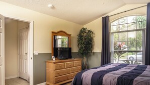 A bedroom with a bed, a dresser, a mirror, and a window with curtains. - 4 Bed Villa - Eagle Pointe - Kissimmee (Kissimmee)