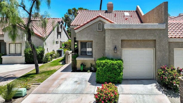 A residential house with a red-tiled roof, a garage, and a well-maintained lawn. - Stylish 2-bedroom condo in Palm Desert with WiFi, AC, and a golf course! (Palm Desert)