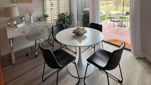 A dining area with a round table, four chairs, a ceiling fan, a white desk with a lamp, a globe, and a vase with flowers. - Stylish 2-bedroom condo in Palm Desert with WiFi, AC, and a golf course! (Palm Desert)