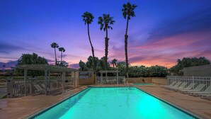 A swimming pool with lounge chairs and a pergola, surrounded by palm trees and a sunset sky. - Stylish 2-bedroom condo in Palm Desert with WiFi, AC, and a golf course! (Palm Desert)