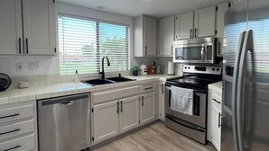 A modern kitchen with white cabinetry, stainless steel appliances, and a wooden floor. - Stylish 2-bedroom condo in Palm Desert with WiFi, AC, and a golf course! (Palm Desert)
