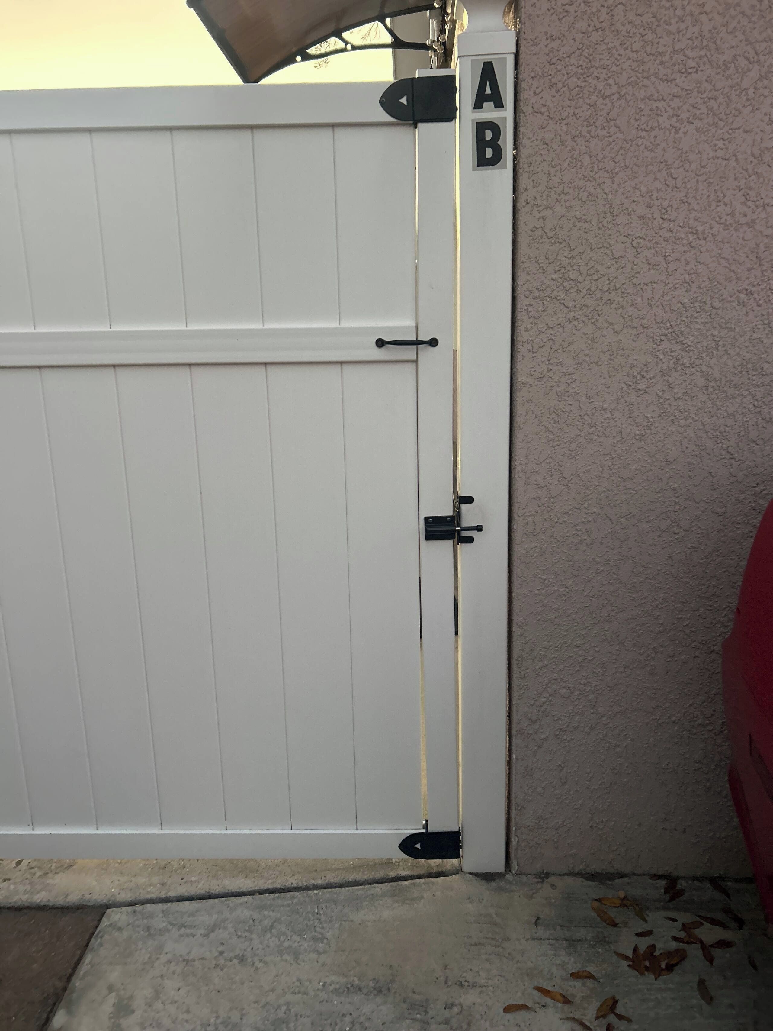 A white gate with a lock, a wall with a textured surface, and a red object partially visible.
