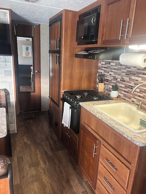 A compact kitchen with wooden cabinets, a built-in microwave, a stove, and a sink.