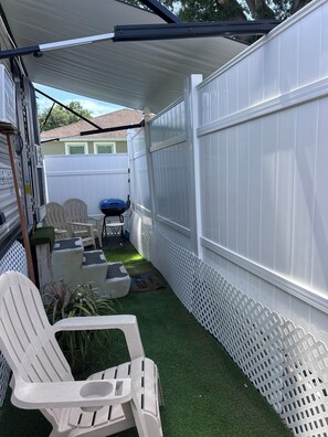 A backyard with a white fence, a covered patio area, and outdoor furniture.