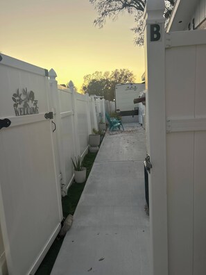 Een omheind pad met een bord van harte welkom, een witte hek en een groen gazon.