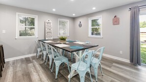 A dining area with a rectangular table, light blue chairs, and a grey wall with windows.