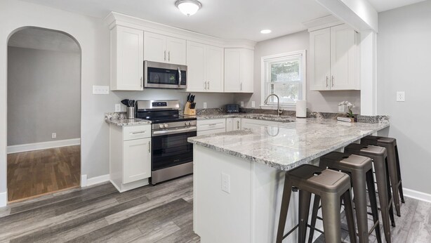 A modern kitchen with white cabinetry, a granite countertop, a built-in oven, and a microwave.