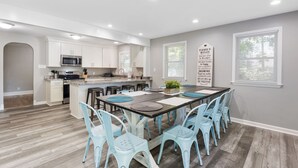 A modern kitchen with white cabinets, a central island, and a dining area with light blue chairs and a large table.