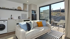 A modern living room with a sofa, a dining table, and a large window offering a view of the outdoors. - Peaceful, Luxury Unit At The Iconic Remarkables! (Queenstown)